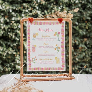 May include: A copper-colored metal framed sign with a watercolor design. The sign displays a menu for a bar, with sections for signature cocktails, beer, wine, and non-alcoholic beverages. The text is in a handwritten style, with floral illustrations.