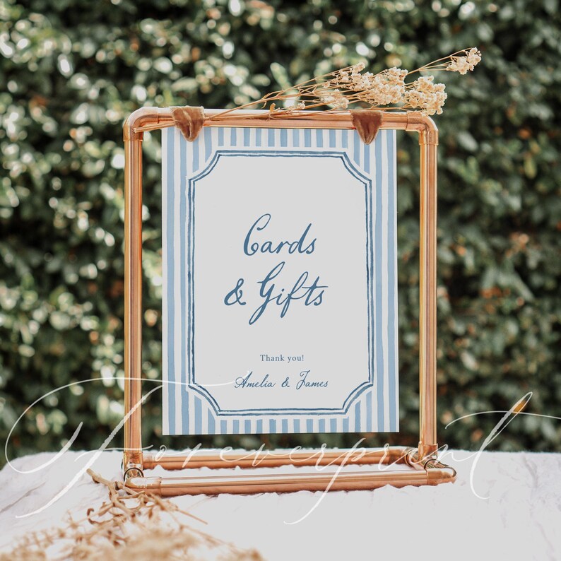 Pu&ograve; includere: Una cornice in metallo color rame sostiene un cartello con sfondo a righe blu e bianche. Il cartello recita "Cards & Gifts" con i nomi "Amelia & James" in basso. Fiori secchi sono posti sopra la cornice.