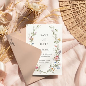 K&ouml;nnte beinhalten: Eine Save-the-Date-Karte mit einem floralen Kranzdesign. Die Karte ist wei&szlig; mit einem hellblauen Rand und Text, der "Save the Date" und "9.06.2024" lautet. Der Text lautet auch "Le & William getting married Tuscany, Italy invitation to follow".