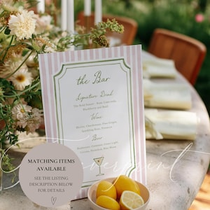 May include: A pink and white striped bar menu with a decorative border, listing signature drinks, wine, and beer options. A small bowl of lemons sits in front of the menu. Text on the menu includes "the Bar" and "Matching Items Available".