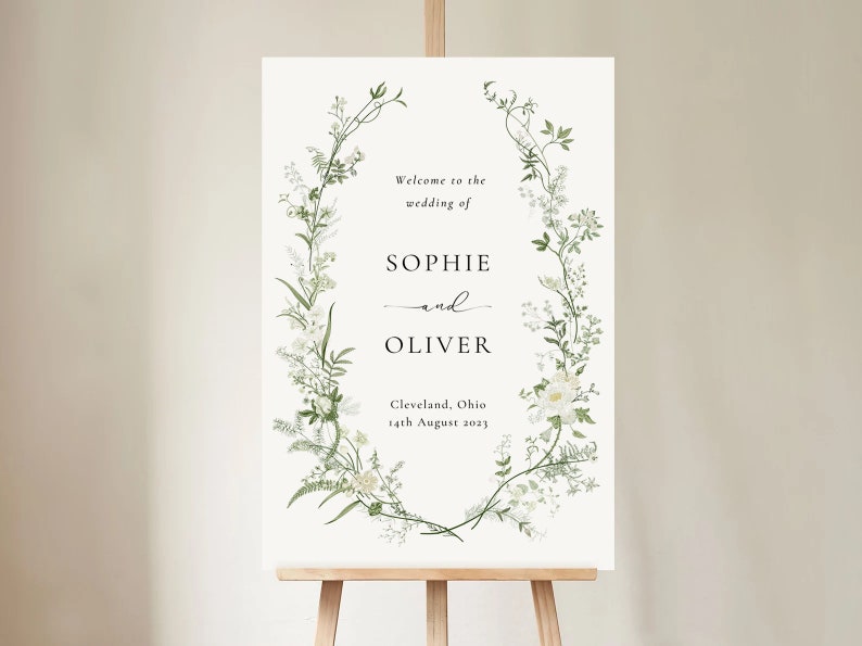 Pode incluir: Um cartaz de boas-vindas de casamento branco com um design de coroa de flores. O cartaz diz "Bem-vindos ao casamento de Sophie e Oliver, Cleveland, Ohio, 14 de agosto de 2023."