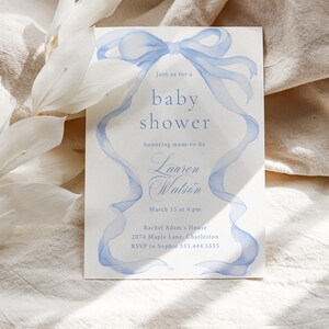 May include: A blue baby shower invitation with a watercolor illustration of a blue ribbon bow. The invitation reads "Join us for a baby shower honoring mom-to-be Lauren Watson March 15 at 4 pm Rachel Adam's House 2074 Maple Lane, Charleston RSVP to Sophie 333.444.5555"
