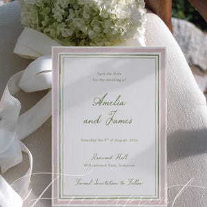 May include: A wedding invitation with a pale pink and green border, featuring the names "Amelia and James" in elegant script. The text "Save the Date" and wedding details are also included. A bouquet of white flowers and a white ribbon are in the background.