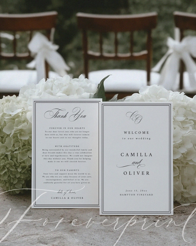 K&ouml;nnte beinhalten: Zwei wei&szlig;e Hochzeitskarten mit schwarzem Text. Auf einer steht "Danke" und auf der anderen "Willkommen zu unserer Hochzeit" mit den Namen Camilla und Oliver. Die Karten sind von wei&szlig;en Blumen umgeben.