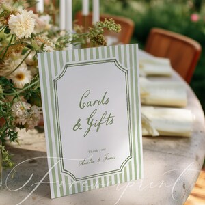 May include: A rectangular sign with green and white striped borders and the words "Cards & Gifts" in elegant script. The sign also includes the names "Amelia & James" and the words "Thank you!" in a wedding setting.
