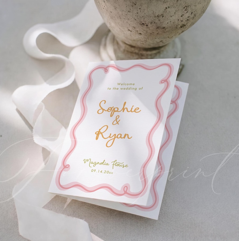 May include: A white wedding invitation card featuring a pink wavy border design. The text reads: Welcome to the wedding of Sophie & Ryan, Magnolia House, 09.14.20xx. The names Sophie and Ryan are printed in a gold script font on the centre of the card.