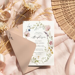 Peut inclure: Une carte d'invitation blanche avec une bordure de couronne florale et une croix dor&eacute;e. Le texte indique "Veuillez nous rejoindre pour c&eacute;l&eacute;brer le bapt&ecirc;me de notre fille Sophie Linnea le 14 ao&ucirc;t 2023 &agrave; l'&eacute;glise St. Mary's, suivi d'un d&eacute;jeuner &agrave; The White House Inn. R&eacute;pondez &agrave; Sophie &agrave; (email uniquement)"