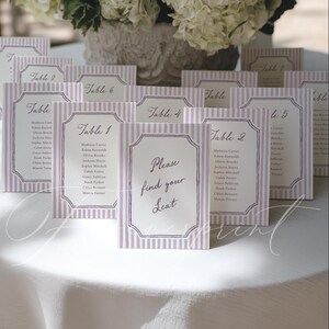 Puede incluir: Una colección de tarjetas de mesa rectangulares verticales con un patrón de rayas verticales en color morado claro y blanco. Cada tarjeta muestra un borde decorativo y texto en negro, incluyendo números de mesa y nombres de invitados, con una tarjeta que dice Please find your seat.