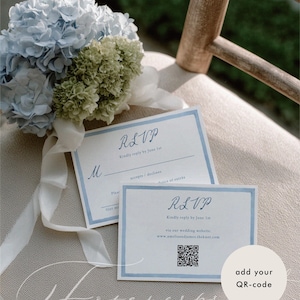 May include: Two RSVP cards with blue borders and text, placed on a neutral surface. The cards have the text "RSVP" and "Kindly reply by June 1st." A QR code is visible on one card. A bouquet of blue and green hydrangeas with white ribbon rests nearby.