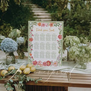 May include: A wooden table displays a floral wedding seating chart with the text "Find your Seat." The chart is surrounded by colorful flowers and greenery. Lemons and floral arrangements in glass vases are also on the table.