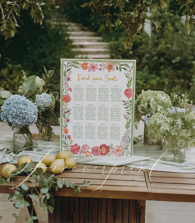 May include: A wooden table displays a floral wedding seating chart with the text "Find your Seat." The chart is surrounded by colorful flowers and greenery. Lemons and floral arrangements in glass vases are also on the table.