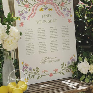 May include: A white seating chart with a floral border and a pink bow. The chart lists eight tables with names for a baby shower. The text at the top reads "Find Your Seat". The text at the bottom reads "Blaire's Baby Shower".