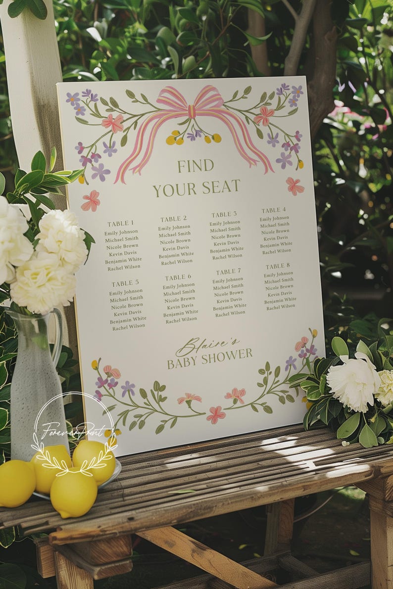 May include: A white seating chart with a floral border and a pink bow. The chart lists eight tables with names for a baby shower. The text at the top reads "Find Your Seat". The text at the bottom reads "Blaire's Baby Shower".