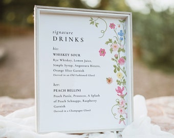 May include: A framed sign with a list of signature drinks for a wedding or event. The sign features a floral design with pink, blue, and yellow flowers. The drinks listed are Whiskey Sour and Peach Bellini.