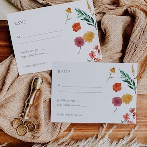 May include: Two white RSVP cards with floral designs. The text on the cards reads "RSVP", "M", "Joyfully accepts", "Regretfully declines", and "Kindly reply by June 1st".
