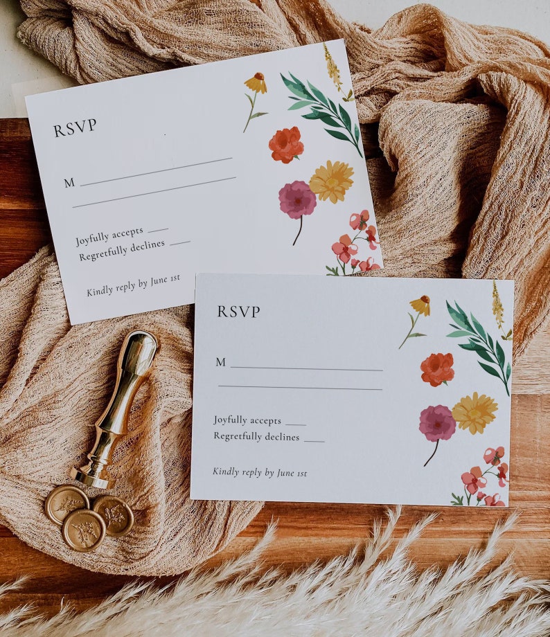 May include: Two white RSVP cards with floral designs. The text on the cards reads "RSVP", "M", "Joyfully accepts", "Regretfully declines", and "Kindly reply by June 1st".