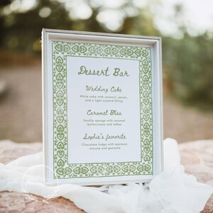 May include: A white framed sign with a green border and the text "Dessert Bar" in green script. The sign lists the wedding cake, caramel bliss, and Sophie's favorite desserts.