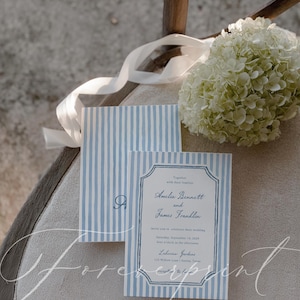 May include: Wedding invitation suite with blue and white striped design. The invitation includes the names Amelia Bennett and James Franklin, along with event details. A white ribbon and a bouquet of white flowers are also present.