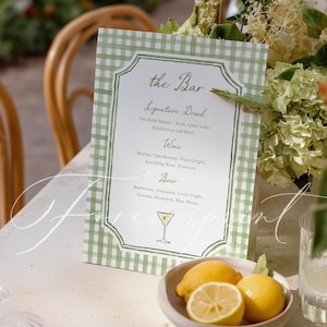 May include: A green and white gingham bar menu with the text "the Bar" and a list of signature drinks, wine, and beer. A small bowl of lemons sits in front of the menu.