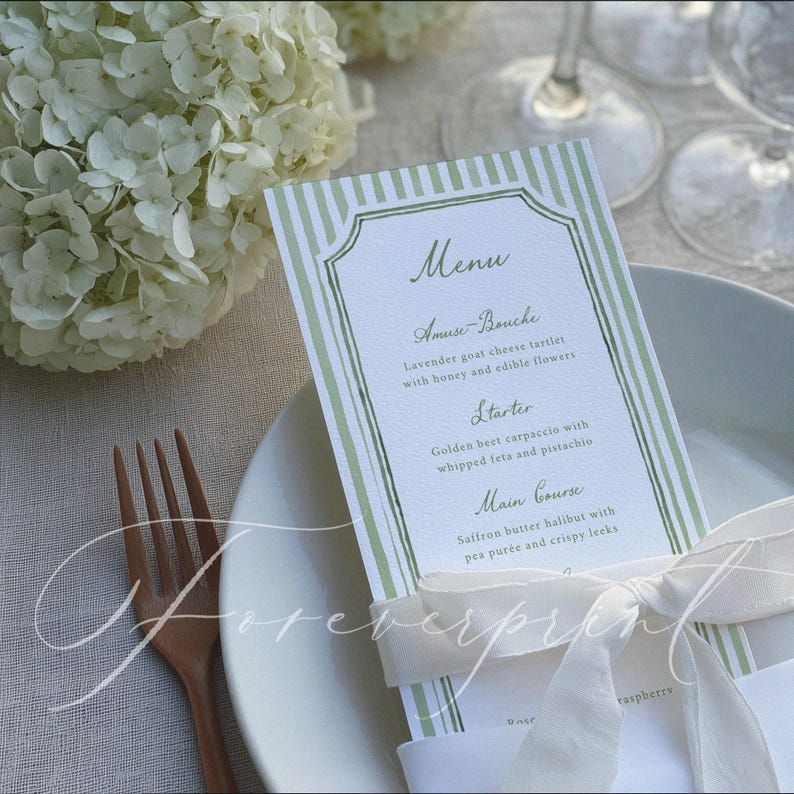 Op de afbeelding: Een menukaart met een groen en wit gestreept ontwerp, met een lijst met gerechten. Het menu bevat een Amuse-Bouche, een Voorgerecht en een Hoofdgerecht. Een wit lint is om de kaart gebonden en een houten vork is zichtbaar.
