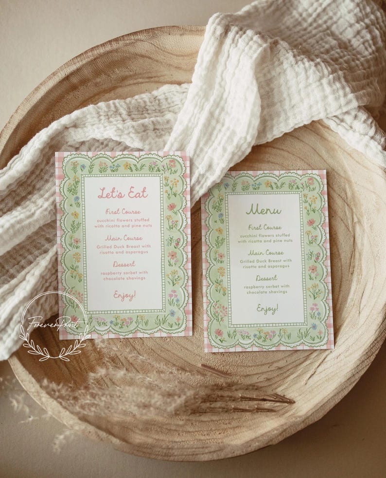 May include: Two floral-bordered menu cards with the text "Let's Eat" and "Menu" on a wooden bowl. The cards have a pink and green color scheme with a floral design. The menu includes first course, main course, and dessert options.