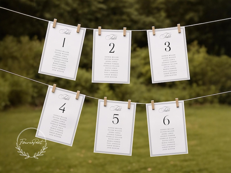 May include: Six white table number cards, numbered 1 through 6, are suspended from a string with wooden clothespins. Each card features a black border, elegant script, and a list of names. The background is a blurred green.