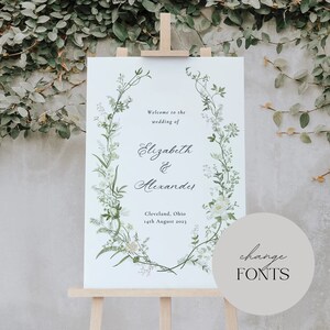 Pode incluir: Um cartaz de casamento branco com uma borda de coroa de flores. O cartaz diz "Bem-vindos ao casamento de Elizabeth & Alexander" e inclui a data e o local: "Cleveland, Ohio 14 de agosto de 2023".