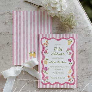 May include: Baby shower invitation with pink and white striped design. The invitation features floral and lemon illustrations, with the text "Baby Shower" and details for Blaire Clarkson's event. A white ribbon and flowers are also present.