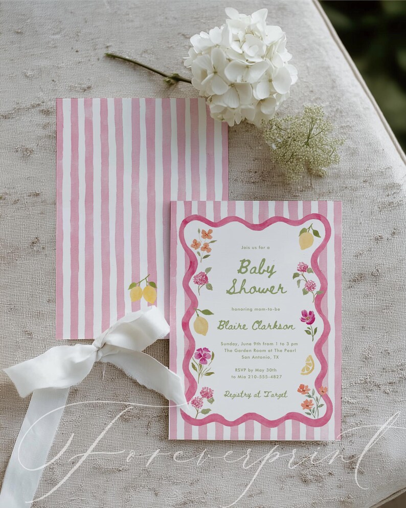 May include: Baby shower invitation with pink and white striped design. The invitation features floral and lemon illustrations, with the text "Baby Shower" and details for Blaire Clarkson's event. A white ribbon and flowers are also present.