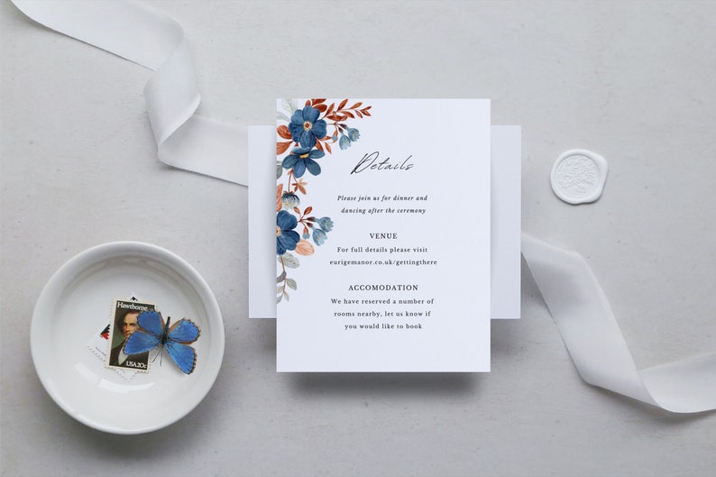 May include: A wedding invitation suite featuring a white card with floral accents in blue and rust colors. The card includes the word "Details" and event information. A white ribbon, a small bowl with a butterfly and a stamp, and a wax seal are also present.