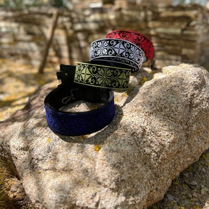 Peut inclure: Quatre sangles tiss&eacute;es avec des motifs de broderie de couleurs diff&eacute;rentes. Les sangles sont noires avec des broderies blanches, rouges et jaunes. Les sangles sont sur un rocher.