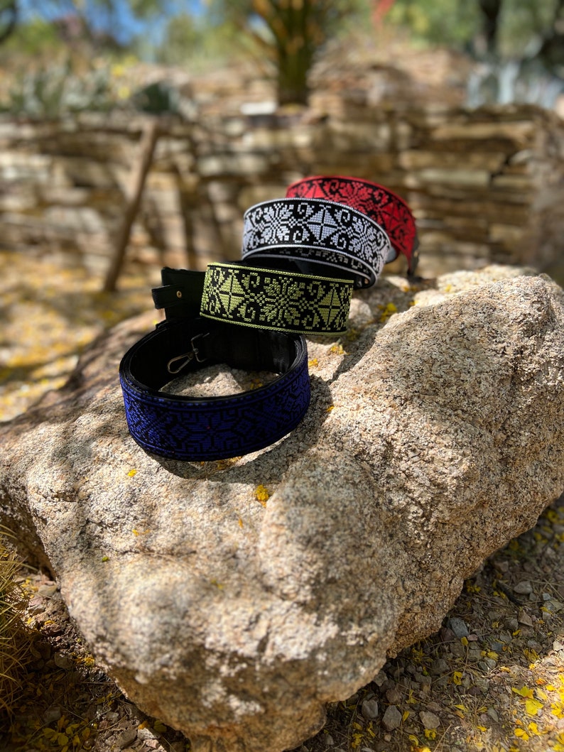 Peut inclure: Quatre sangles tiss&eacute;es avec des motifs de broderie de couleurs diff&eacute;rentes. Les sangles sont noires avec des broderies blanches, rouges et jaunes. Les sangles sont sur un rocher.
