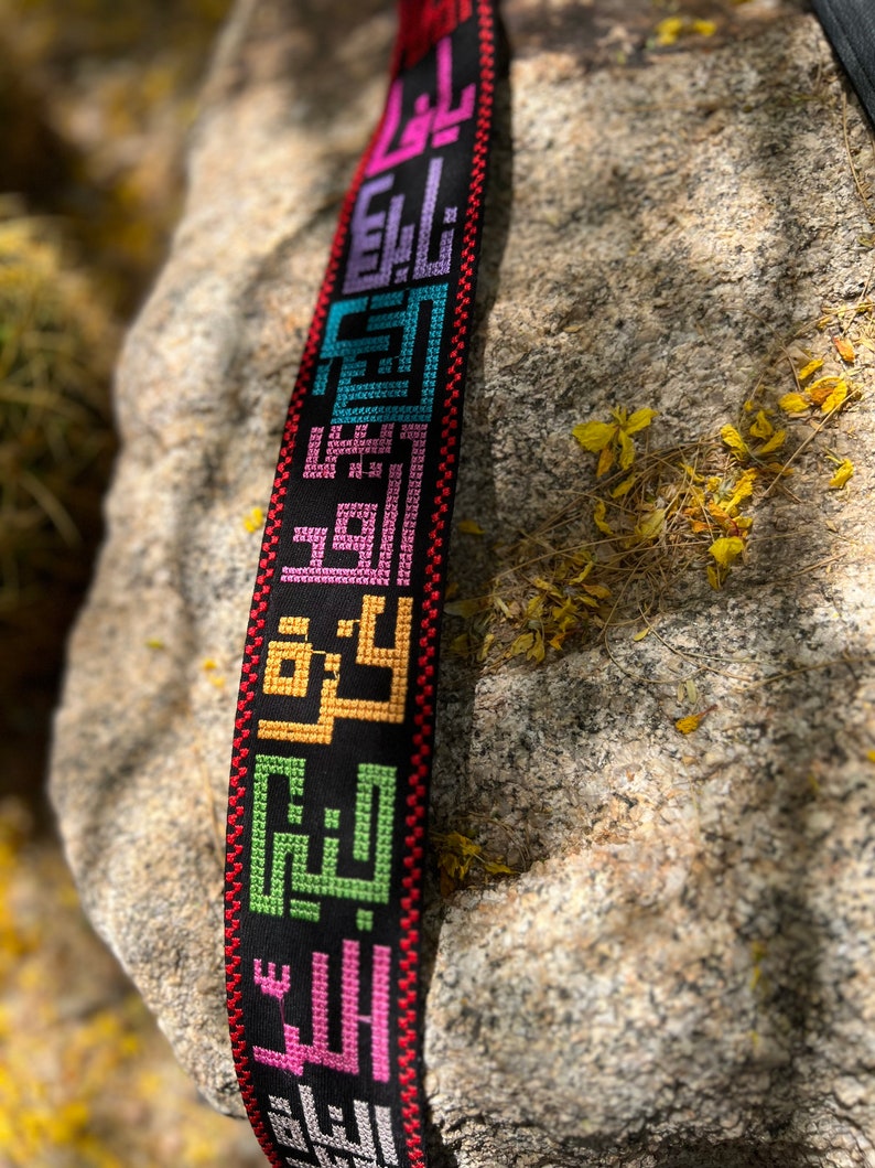 Peut inclure: Une sangle tiss&eacute;e noire avec des inscriptions arabes brod&eacute;es color&eacute;es. La sangle est faite d'un mat&eacute;riau &eacute;pais et durable et a une bordure rouge.