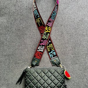 Peut inclure: Un sac &agrave; bandouli&egrave;re matelass&eacute; noir avec une bandouli&egrave;re noire et multicolore orn&eacute;e d'&eacute;criture arabe. Le sac a un charme past&egrave;que attach&eacute; &agrave; lui.
