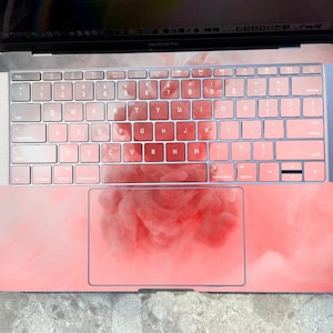 May include: A pink laptop computer with a white keyboard and a pink and white cloud design on the trackpad.