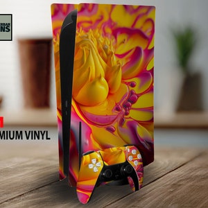 May include: A PlayStation 5 console and controller skin with a bright abstract pattern in yellow, pink, and orange. The console skin is applied to the side panels, and the controller skin covers the front. The text "3M Premium Vinyl" is visible.