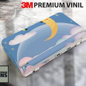 Könnte beinhalten: Eine Hülle für eine Handheld-Spielkonsole mit einem skurrilen Design mit Mond, Sternen und Wolken auf blauem Hintergrund. Die Hülle ist mit "3M Premium Vinil" beschriftet und enthält das Logo "Wunderbar Skins".