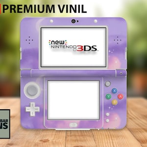 May include: A purple New Nintendo 3DS console with a custom skin featuring a watercolor sky design. The console has a white screen and the text "new Nintendo 3DS". The top of the console has the text "3M Premium Vinil".