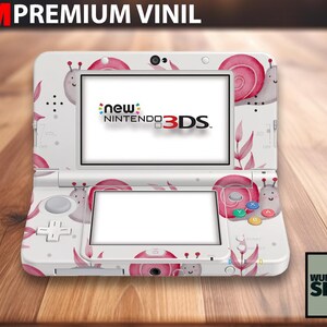 May include: White New Nintendo 3DS console skin with a whimsical design featuring pink snails and leaves. The console has a screen and buttons, with the text "new Nintendo 3DS" visible on the screen. The skin is labeled "3M Premium Vinyl".