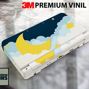 Puede incluir: Consola de juegos portátil blanca con una piel personalizada con un diseño de cielo nocturno. La piel incluye una luna creciente amarilla, estrellas y nubes sobre un fondo azul marino. El texto "3M PREMIUM VINIL" está en la parte superior.