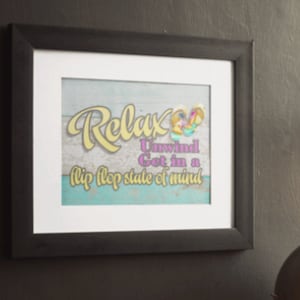 Puede incluir: Una impresión enmarcada con un diseño de playa. El texto dice "Relax Unwind Get in a flip flop state of mind".