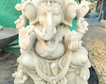 Op de afbeelding: Wit marmeren beeld van de hindoeïstische god Ganesha, zittend met zijn slurf omhoog en een kom in zijn hand. Het beeld is ingewikkeld gebeeldhouwd met details op de kleding en hoofdtooi.