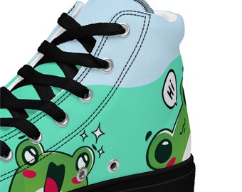 Op de afbeelding: Hoge canvas schoenen met een zwarte zool en een blauw en groen ontwerp met cartoon kikkers. Eén kikker zegt "Hoi!" in een spraakballon.