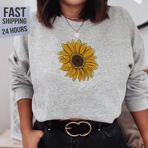 May include: A gray sweatshirt with a yellow sunflower graphic on the front. The sunflower has a brown center and yellow petals.