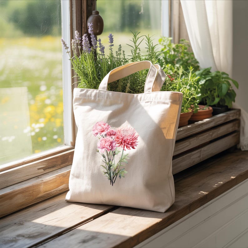 A white tote bag with a floral design is placed on a wooden windowsill, with a potted plant and flowers visible through the window.