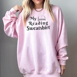 May include: A pink sweatshirt with the text "My Reading Sweatshirt" and a black and white illustration of an open book.