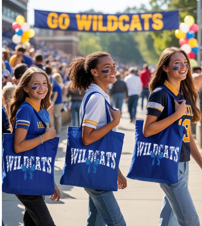 Three young women wearing blue and yellow "Wildcats" shirts and carrying blue bags with the same "Wildcats" text are walking together, smiling and enjoying the event.