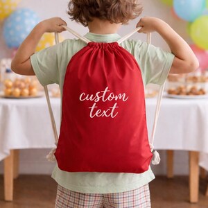 A young child wearing a red backpack with the text "custom text" printed on it, standing in front of a table with colorful balloons.