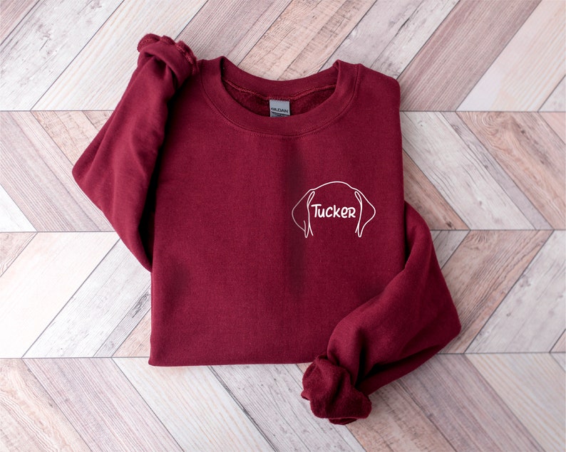 May include: Burgundy sweatshirt with a white outline of a dog's head and the name "Tucker" written inside.