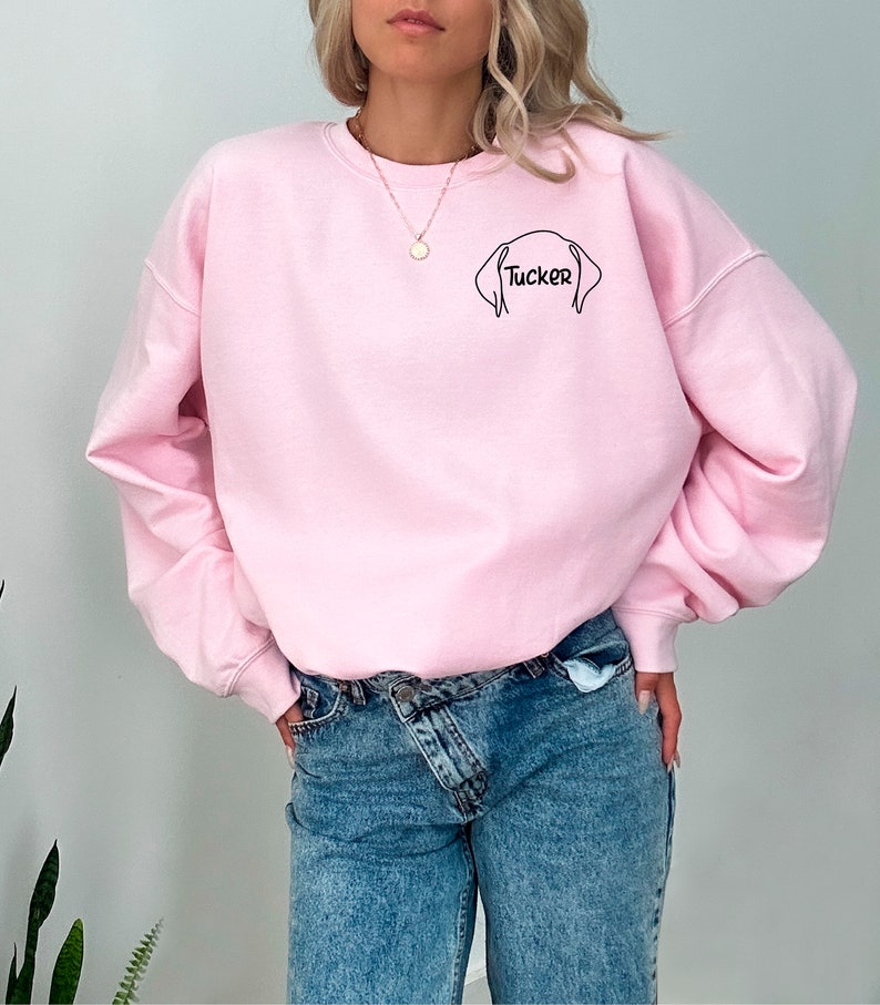 May include: A pink sweatshirt with a black outline of a dog's head and the name "Tucker" written underneath.